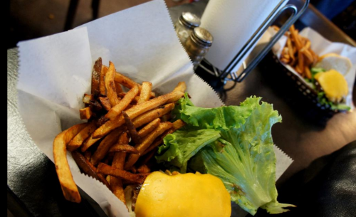 A plate with a cheeseburger, lettuce, and a side of crispy French fries on a table.
