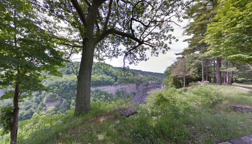 A scenic view of a lush green landscape with a steep cliff and trees, under a clear sky.