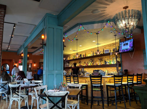 A cozy restaurant interior with colorful lights, a bar, and tables set for dining. People are enjoying their meals.