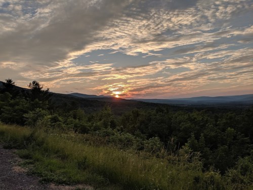 A scenic sunset over rolling hills, with vibrant clouds and lush greenery in the foreground.