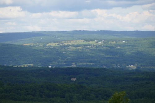 A panoramic view of rolling green hills and fields under a cloudy sky.