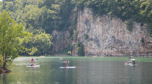 People paddleboarding on a calm lake surrounded by lush greenery and steep rocky cliffs.