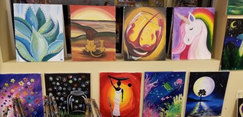 A colorful display of various paintings, including landscapes, animals, and abstract art, arranged on a wall.