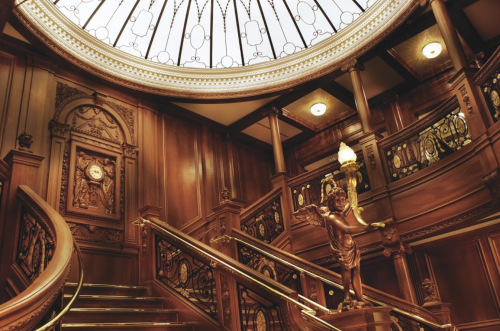 Elegant wooden staircase with ornate railings and a glass dome ceiling, featuring a decorative statue.