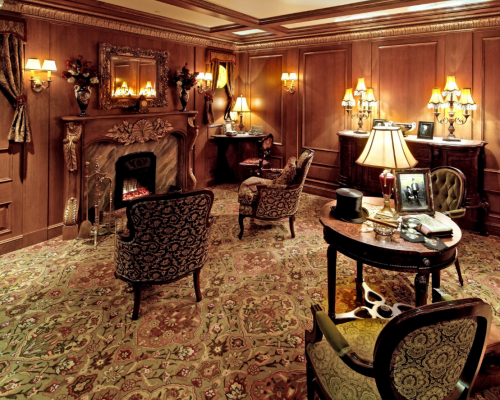 Cozy, elegant room with wooden walls, vintage furniture, a fireplace, and warm lighting. Richly patterned carpet.