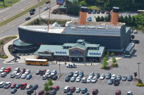 A large replica of a ship resembling the Titanic sits atop a building, surrounded by a parking lot filled with cars.