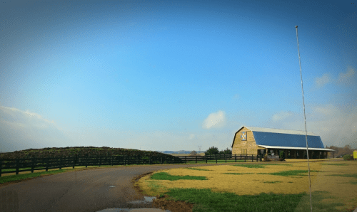 A scenic view of a barn beside a gravel road, with a blue sky and green fields in the background.