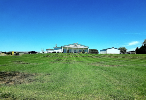 A large, well-maintained house on a grassy lawn under a clear blue sky, with a shed nearby.