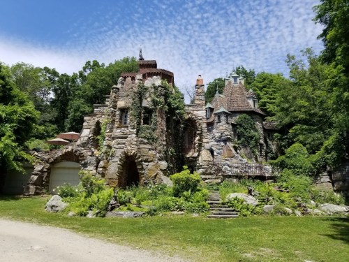 A whimsical stone castle covered in greenery, surrounded by lush trees and a clear blue sky.