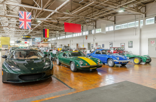 A collection of classic cars displayed in a spacious showroom with flags hanging from the ceiling.