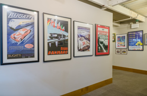 A gallery wall featuring vintage car posters, including Bugatti and Panhard, in a well-lit space.
