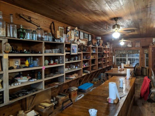 A rustic interior of a cozy shop with wooden shelves filled with vintage items and a long wooden counter.