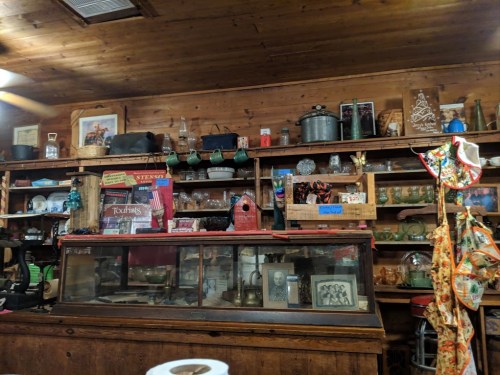 A rustic wooden shelf filled with vintage items, glassware, and antiques in a cozy, dimly lit space.