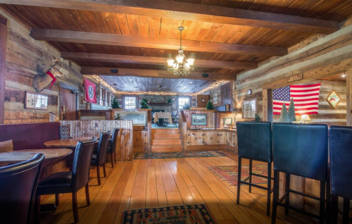 Cozy rustic interior of a restaurant with wooden beams, tables, and American flags on the walls. Warm lighting.