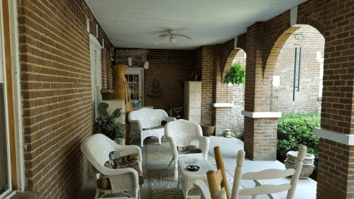 A cozy porch with wicker chairs, potted plants, and brick arches, creating a welcoming outdoor space.