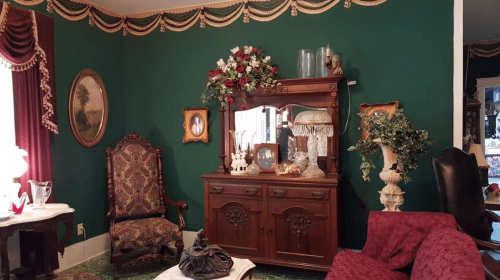 A vintage room with green walls, ornate furniture, floral decor, and a cozy seating area.