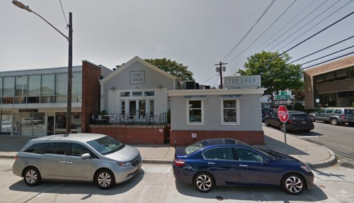 Exterior view of a restaurant called "The Shed," with parked cars and street signs in a suburban setting.