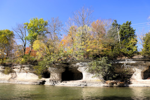 Scenic riverbank with rocky cliffs and colorful autumn trees under a clear blue sky.