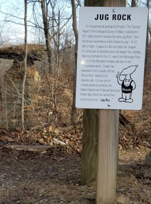 Sign about Jug Rock, a natural rock formation in Pennsylvania, with trees and a rocky landscape in the background.