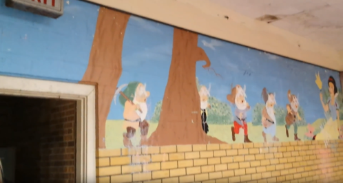 Mural of cartoon characters in a forest, featuring whimsical figures near trees and a bright blue sky.