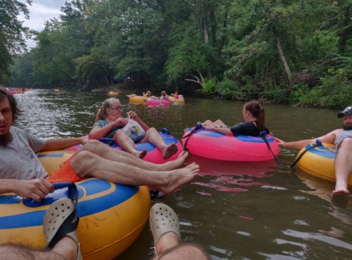 Group of people relaxing on colorful inner tubes in a river, surrounded by lush greenery.