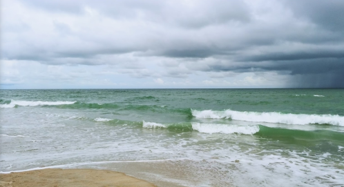 A serene beach scene with gentle waves, under a cloudy sky with hints of sunlight peeking through.