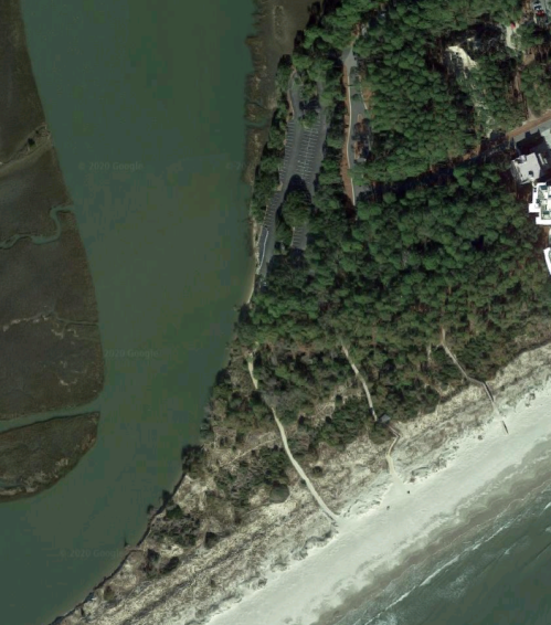 Aerial view of a coastal area with greenery, a beach, and a winding path along the shoreline.