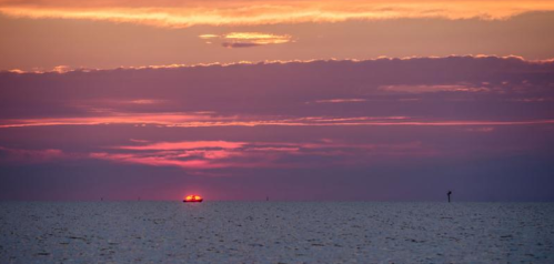 A serene sunset over the ocean, with a boat silhouetted against vibrant pink and purple clouds.