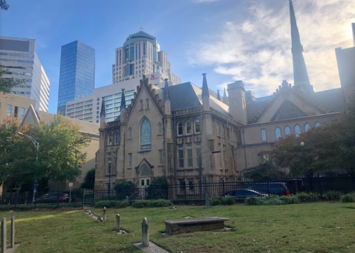 Historic church building with modern skyscrapers in the background, surrounded by greenery and a clear blue sky.