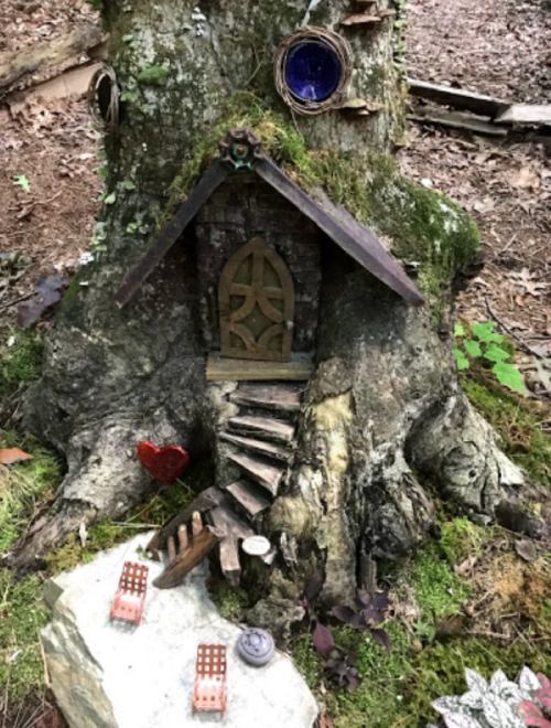 A whimsical miniature house built into a tree trunk, surrounded by moss and small decorative items.