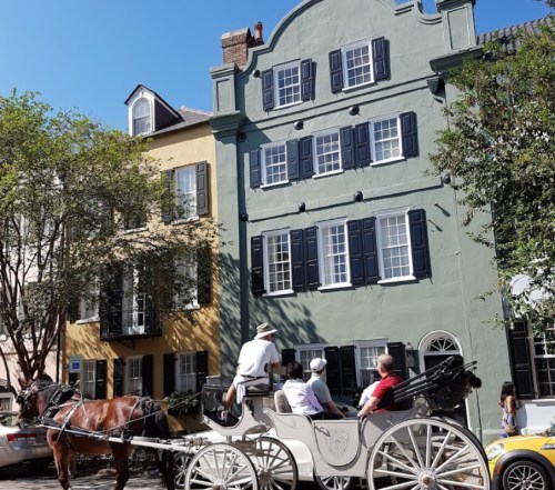 A horse-drawn carriage passes by colorful historic buildings under a clear blue sky.