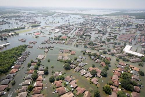 Aerial view of a flooded residential area, with homes partially submerged in water and surrounding landscape affected by flooding.