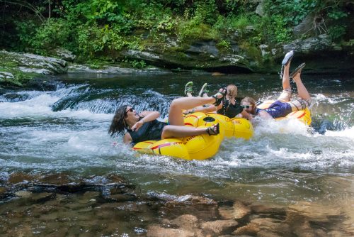 Three people in yellow inner tubes float down a rocky river, splashing water and enjoying a sunny day.