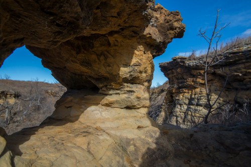 Rock formations under a clear blue sky, with dry vegetation and rugged terrain in the background.