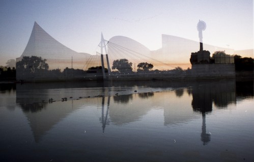 A serene river scene at sunset, featuring reflections of modern architecture and silhouettes of trees.