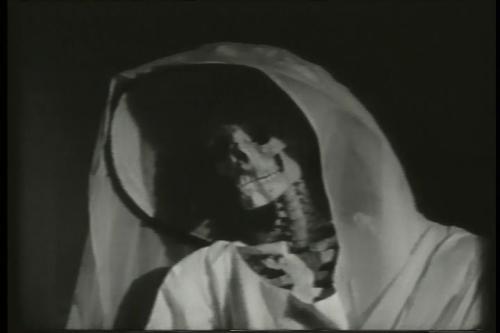 A cloaked skeleton with a hood, appearing ominous in a black and white setting.