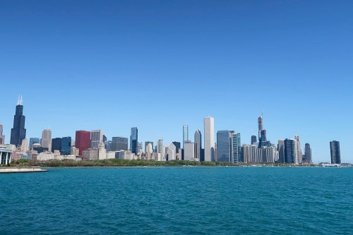 Panoramic view of Chicago skyline with skyscrapers against a clear blue sky, reflecting in the water.