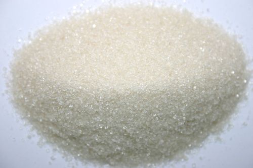 A close-up of a mound of white granulated sugar on a light background.