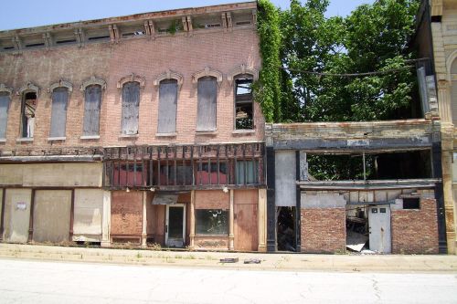 Abandoned buildings with boarded windows and overgrown vegetation, showcasing urban decay and neglect.