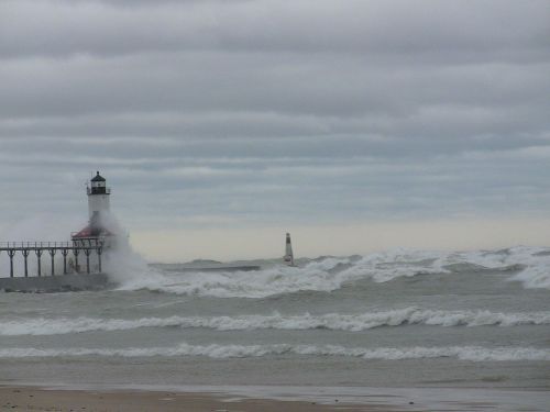 A lighthouse stands near a turbulent sea with large waves under a cloudy sky.
