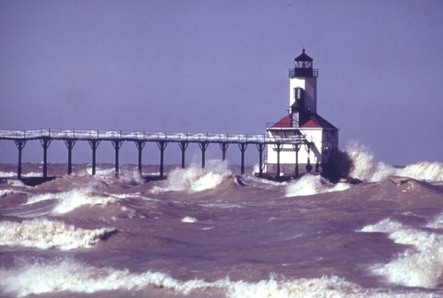 A lighthouse stands on a pier amidst turbulent waves and a stormy sky.