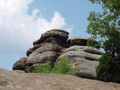 Rock formations under a blue sky with scattered clouds, surrounded by greenery.