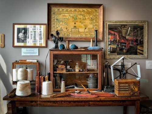 A vintage display featuring textile tools, spools of thread, and historical maps in a museum setting.