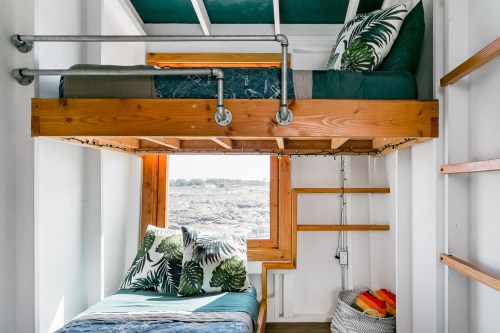 Cozy bedroom with a lofted bed, wooden accents, and tropical-themed bedding, featuring a window with a scenic view.
