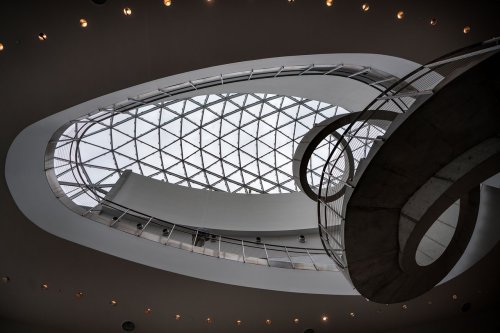 A modern architectural interior featuring a spiral staircase and a large, geometric glass ceiling.