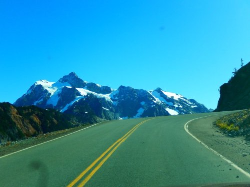A winding road leads towards snow-capped mountains under a clear blue sky.