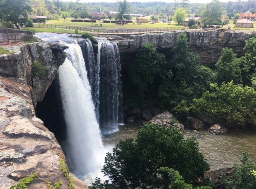 A scenic waterfall cascading over a rocky cliff, surrounded by lush greenery and a calm river below.