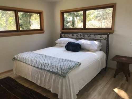Cozy bedroom featuring a bed with white linens, a blue throw, and large windows overlooking greenery.
