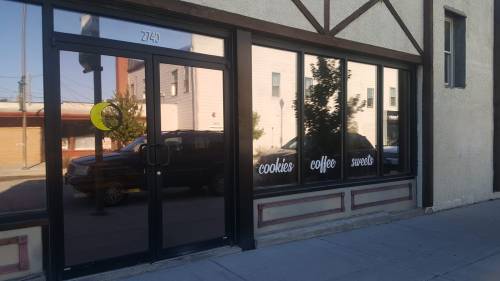 A storefront with large windows displaying the words "cookies," "coffee," and "sweets," reflecting the street outside.
