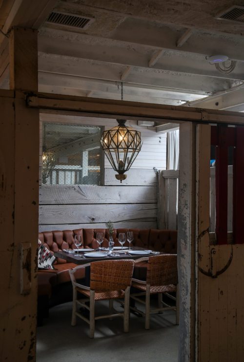 Cozy restaurant interior with a wooden booth, elegant table settings, and a vintage pendant light.